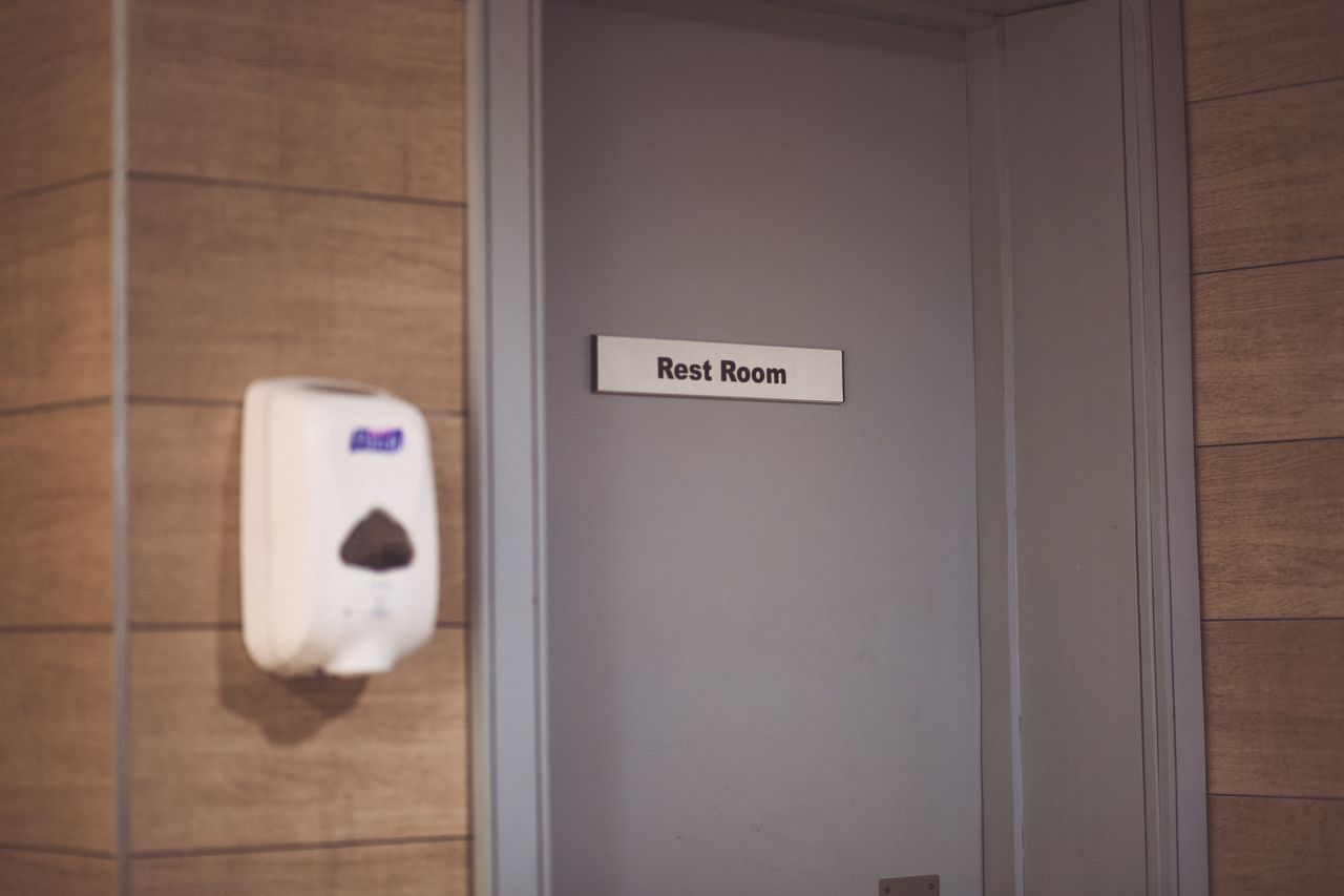 Image of a soap dispenser and a restroom door sign in a public restroom.